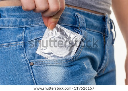 the hand of a young woman pulling a condom to prevent pregnancy from her jeans pocket - stock photo