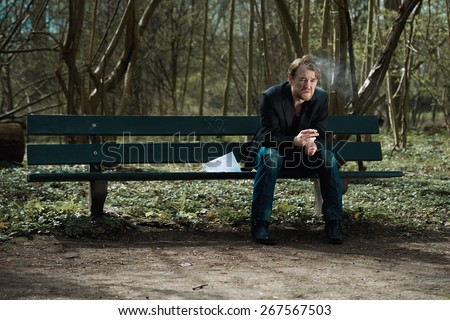 stock-photo-a-well-dressed-depressed-man-sitting-on-a-bench-in-a-park-smoking-a-cigarette-with-a-suicide-note-267567503.jpg