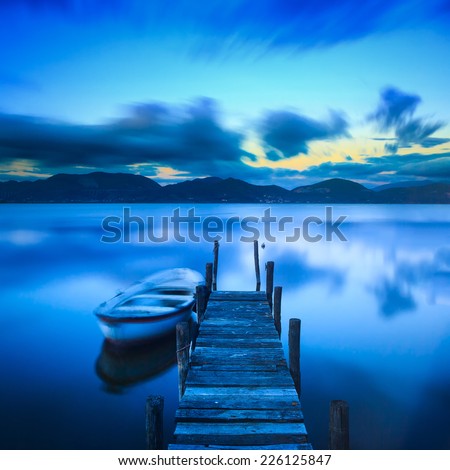 Wooden pier or jetty and a boat on lake sunset and sky reflection 