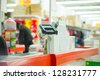 Empty cash desk with payment terminal and customers in queue in supermarket - stock photo