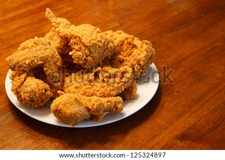 Fresh fried chicken on a white plate set on a wood table - stock photo