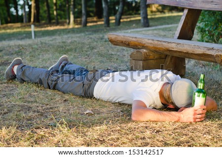 Drunk man sleeping it off in a park lying on his stomach on the ground ...