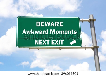 Green overhead road sign with a Beware Awkward Moments Next Exit concept against a partly cloudy sky background. - stock photo