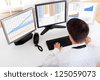 Over the shoulder view of the computer screens of a stock broker trading in a bull market showing ascending graphs - stock photo